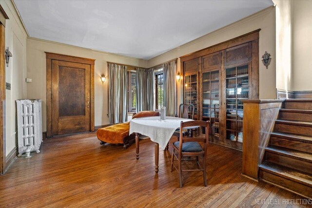 dining space featuring radiator, wood finished floors, crown molding, and stairs