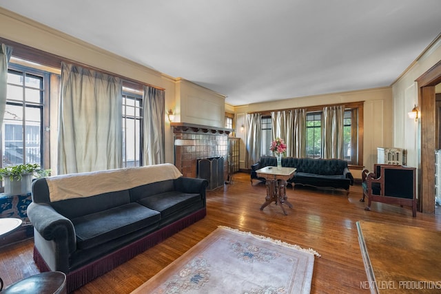 living room featuring plenty of natural light, a tile fireplace, wood finished floors, and crown molding