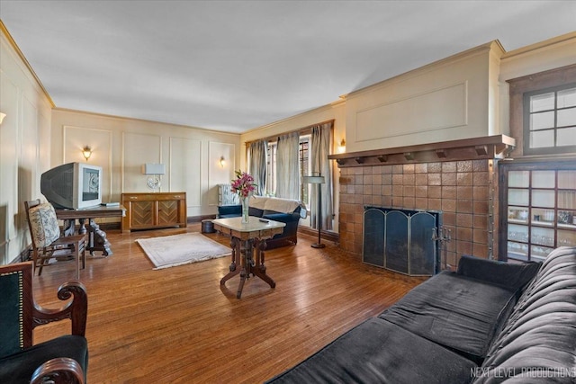 living room featuring a decorative wall, crown molding, a tiled fireplace, and wood finished floors