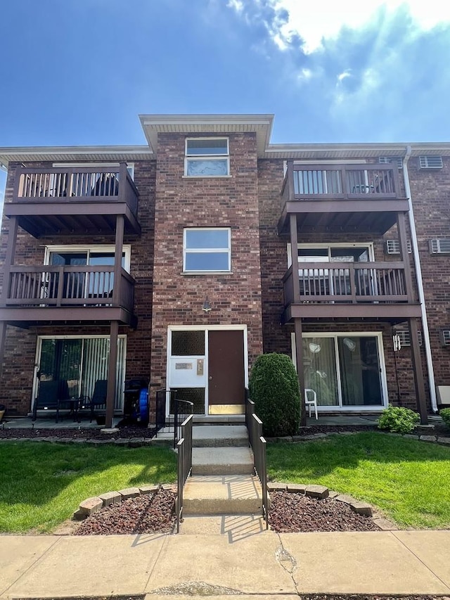 view of front of property featuring a balcony, brick siding, and a front yard