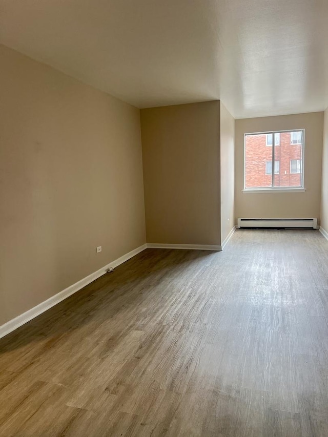 empty room featuring a baseboard heating unit, baseboards, and wood finished floors