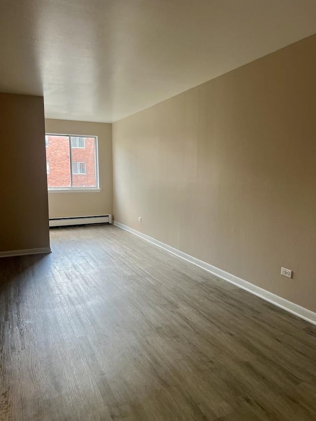 empty room featuring a baseboard heating unit, wood finished floors, and baseboards