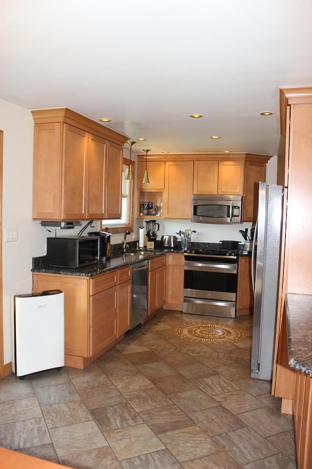 kitchen with appliances with stainless steel finishes, stone finish flooring, a sink, recessed lighting, and dark stone counters
