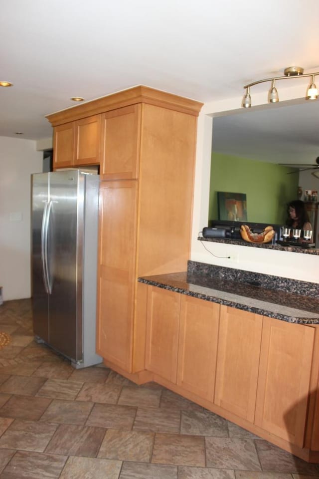 kitchen with freestanding refrigerator, dark stone counters, ceiling fan, and light stone finish floors