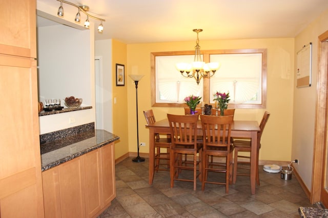 dining room featuring a chandelier, stone finish floors, and baseboards