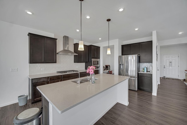 kitchen featuring wall chimney exhaust hood, appliances with stainless steel finishes, a sink, decorative backsplash, and a center island with sink