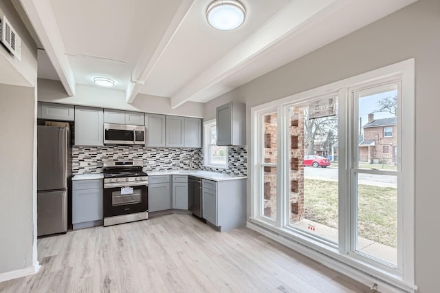 kitchen with stainless steel appliances, gray cabinetry, tasteful backsplash, light wood-style floors, and light countertops