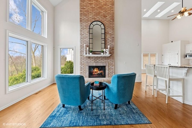 21827 W Riviera Ct, Ivanhoe, IL 60060 - sitting room featuring high vaulted ceiling, light wood finished floors, a fireplace, ceiling fan, and baseboards