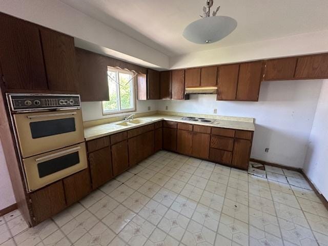 kitchen featuring a sink, light countertops, under cabinet range hood, white appliances, and baseboards