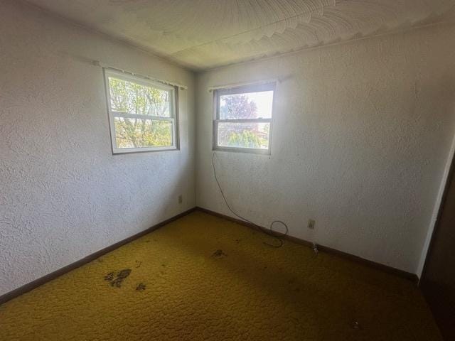 empty room with carpet flooring, a textured wall, and baseboards