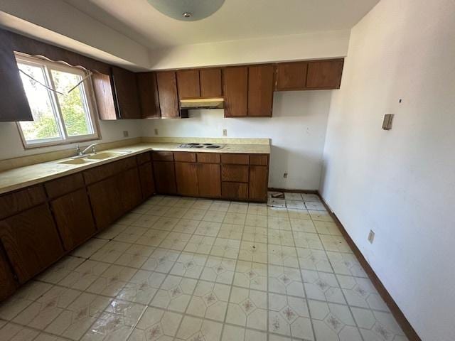 kitchen featuring a sink, under cabinet range hood, baseboards, light countertops, and stovetop