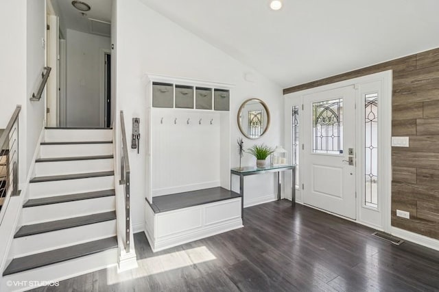 entrance foyer with vaulted ceiling, wooden walls, dark wood-style floors, and stairs