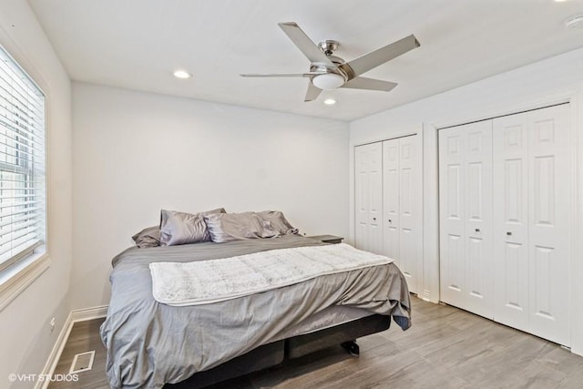 bedroom with light wood finished floors, two closets, recessed lighting, ceiling fan, and baseboards
