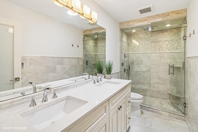 full bath featuring tile walls, a stall shower, double vanity, and toilet