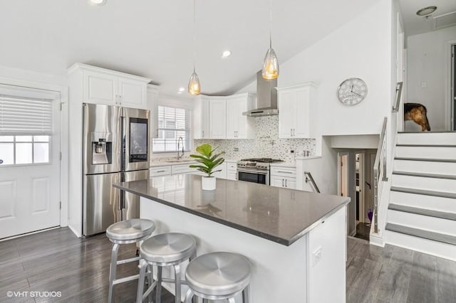 kitchen with appliances with stainless steel finishes, wall chimney exhaust hood, decorative backsplash, vaulted ceiling, and white cabinetry