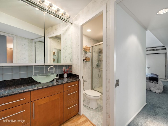 ensuite bathroom with a stall shower, toilet, vanity, and backsplash