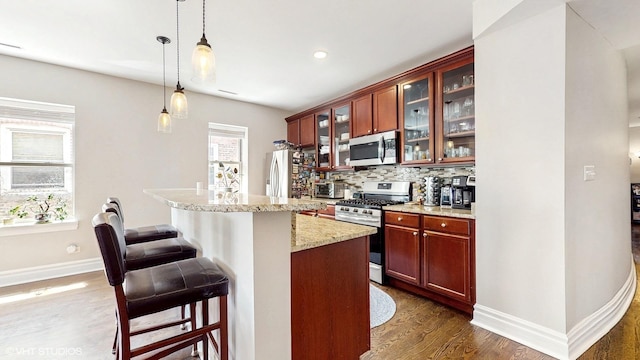 kitchen with appliances with stainless steel finishes, a breakfast bar, decorative backsplash, dark wood-style floors, and hanging light fixtures