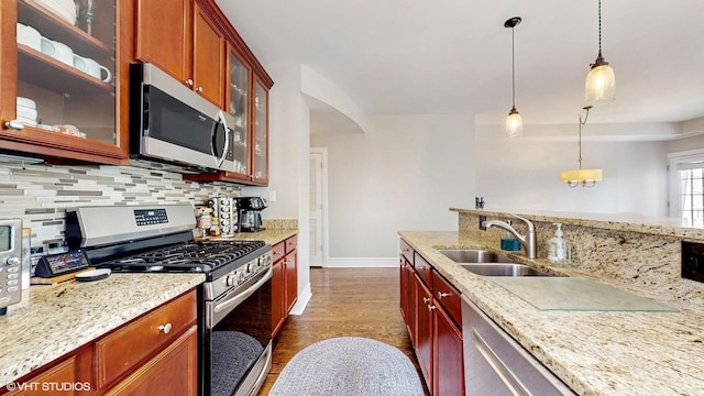kitchen with stainless steel appliances, a sink, backsplash, dark wood-style flooring, and hanging light fixtures