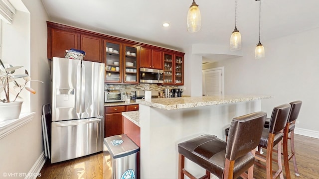 kitchen with stainless steel appliances, wood finished floors, pendant lighting, tasteful backsplash, and recessed lighting
