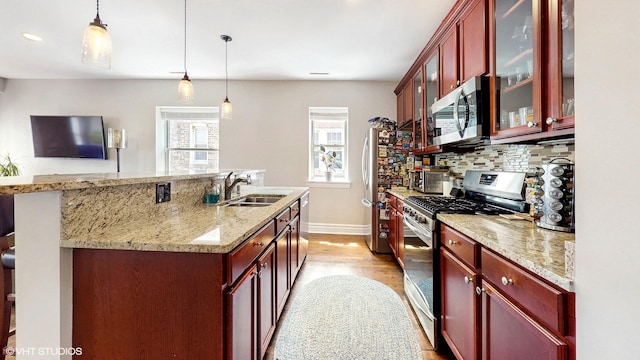 kitchen featuring stainless steel appliances, reddish brown cabinets, a sink, wood finished floors, and a kitchen island with sink