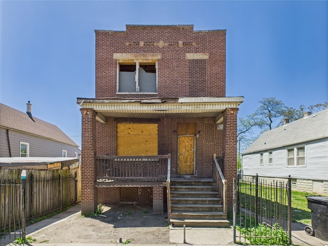 view of front facade featuring brick siding, a porch, and fence