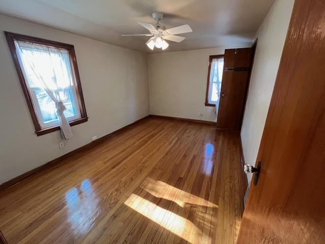 unfurnished bedroom with multiple windows, wood finished floors, baseboards, and a ceiling fan