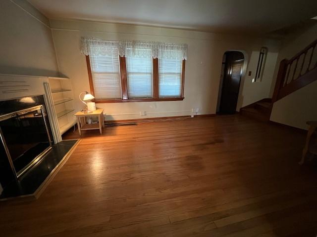 unfurnished living room with a fireplace with raised hearth, wood finished floors, and arched walkways