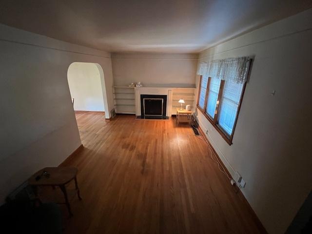 unfurnished living room featuring a fireplace with flush hearth, arched walkways, and wood finished floors