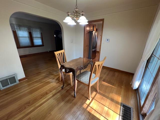 dining room with arched walkways, a chandelier, wood finished floors, and baseboards