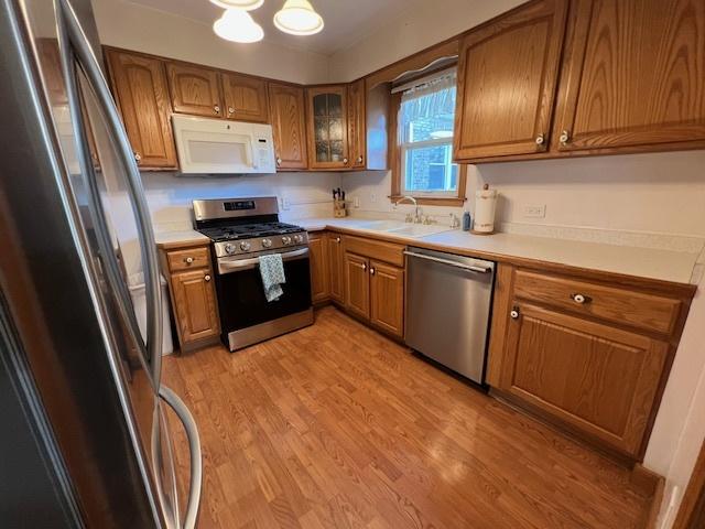 kitchen with stainless steel appliances, brown cabinetry, a sink, light countertops, and light wood finished floors