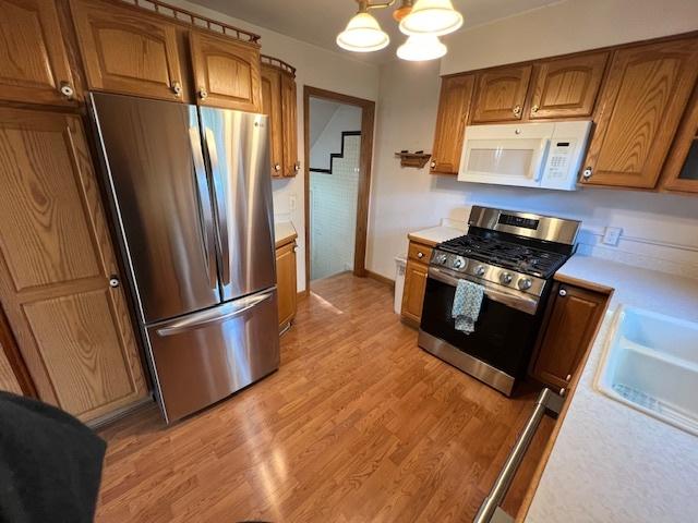 kitchen featuring stainless steel appliances, light countertops, a chandelier, brown cabinets, and light wood-style floors