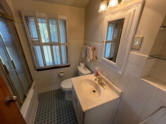 full bath with tile walls, toilet, vanity, a wainscoted wall, and enclosed tub / shower combo