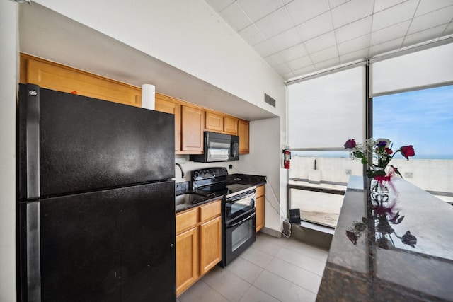 kitchen with black appliances, tile patterned flooring, a sink, and dark stone counters