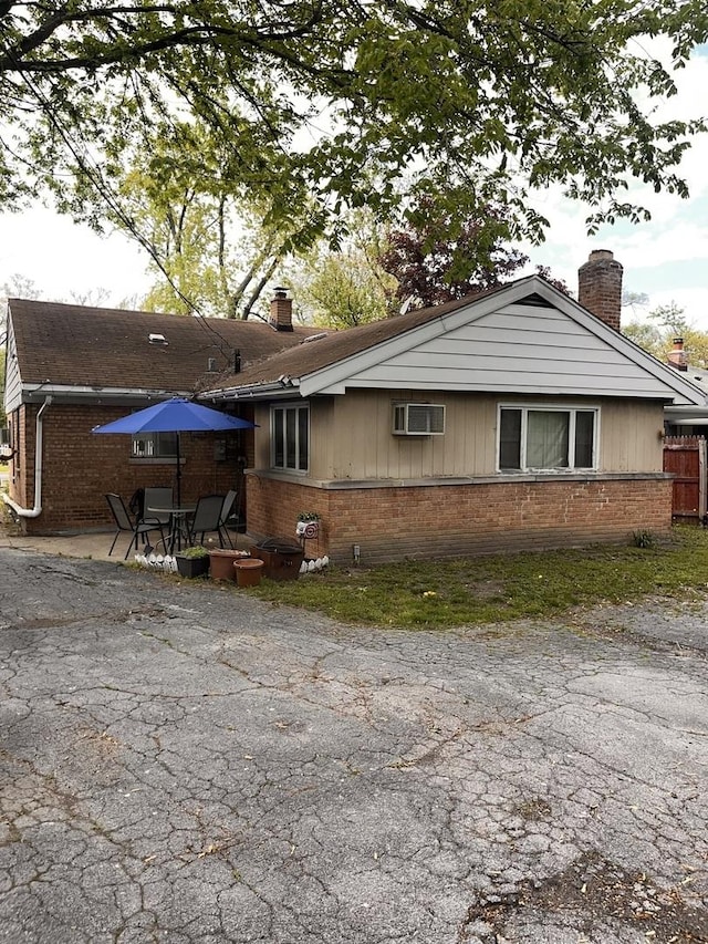 view of front of property featuring brick siding, a chimney, a patio, and a wall mounted air conditioner