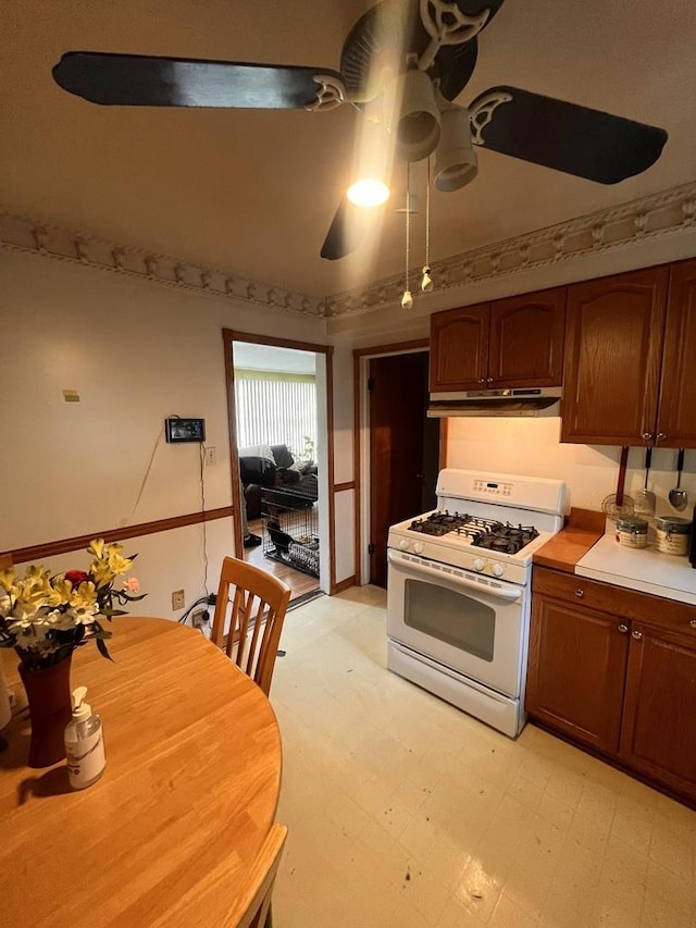 kitchen with white range with gas cooktop, under cabinet range hood, light floors, ceiling fan, and light countertops