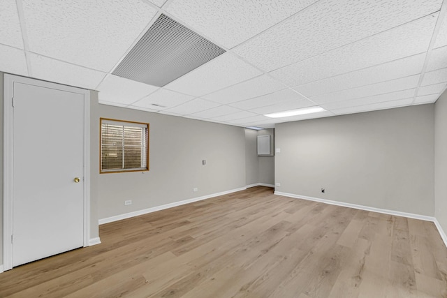 finished below grade area featuring a drop ceiling, baseboards, and light wood-style floors