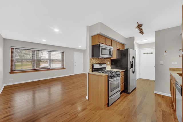 kitchen with stainless steel appliances, light wood-style flooring, decorative backsplash, open floor plan, and baseboards