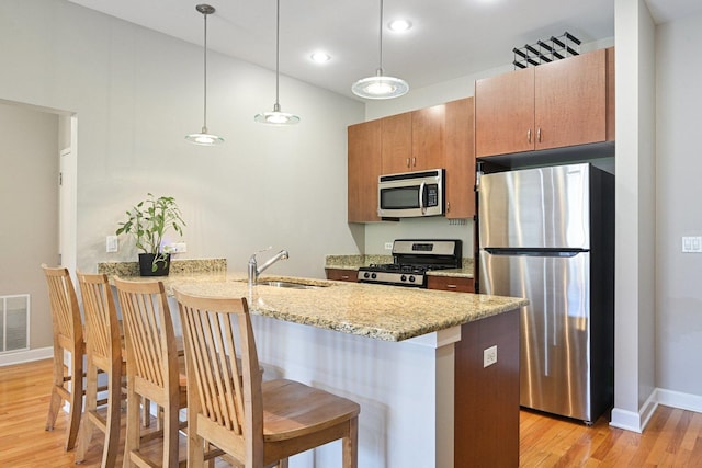 kitchen with appliances with stainless steel finishes, a sink, light wood finished floors, a peninsula, and recessed lighting