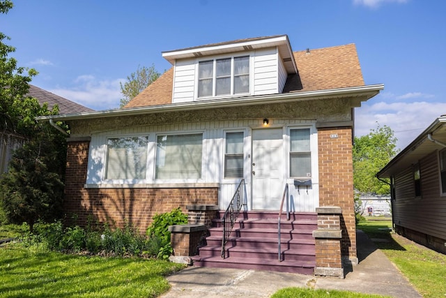bungalow featuring entry steps, brick siding, and a shingled roof