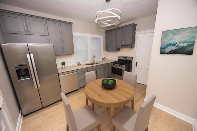kitchen with appliances with stainless steel finishes, a sink, a chandelier, light wood-style floors, and under cabinet range hood