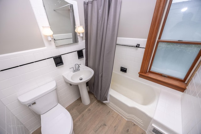 bathroom featuring wood finished floors, tile walls, toilet, a wainscoted wall, and shower / bath combo