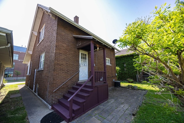 back of property featuring brick siding, a chimney, central air condition unit, and a patio