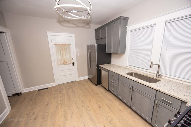 kitchen with a sink, stainless steel appliances, gray cabinets, a chandelier, and light wood finished floors