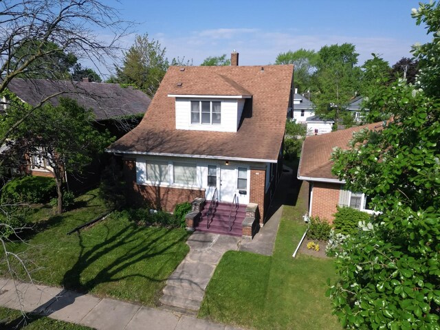 bungalow-style house featuring brick siding, a chimney, and a front lawn