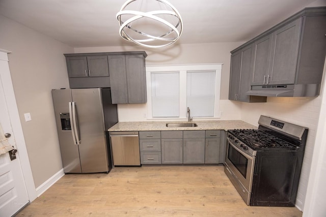 kitchen featuring appliances with stainless steel finishes, a sink, under cabinet range hood, light wood-style floors, and hanging light fixtures