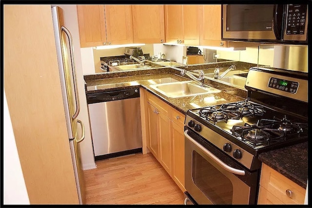 kitchen featuring appliances with stainless steel finishes, a sink, dark countertops, and light wood finished floors