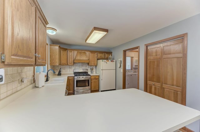 kitchen with stainless steel range with gas cooktop, freestanding refrigerator, a sink, light countertops, and backsplash