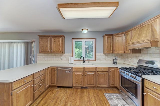 kitchen with stainless steel appliances, a sink, a peninsula, light countertops, and light wood-style floors