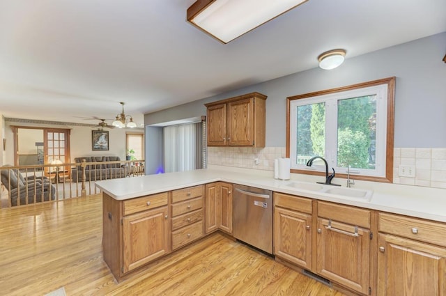 kitchen with stainless steel dishwasher, a sink, a peninsula, and light countertops