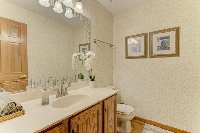 bathroom with wallpapered walls, toilet, wood finished floors, and vanity